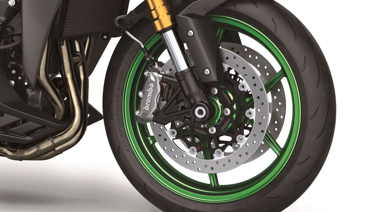 Close-up of a sport motorcycle front wheel showing a green alloy rim, perforated brake disc, and a Brembo caliper near the suspension fork