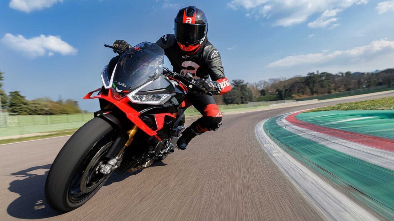 Rider in full protective gear leaning into a sharp turn on a red-and-black sport motorcycle on a race track.