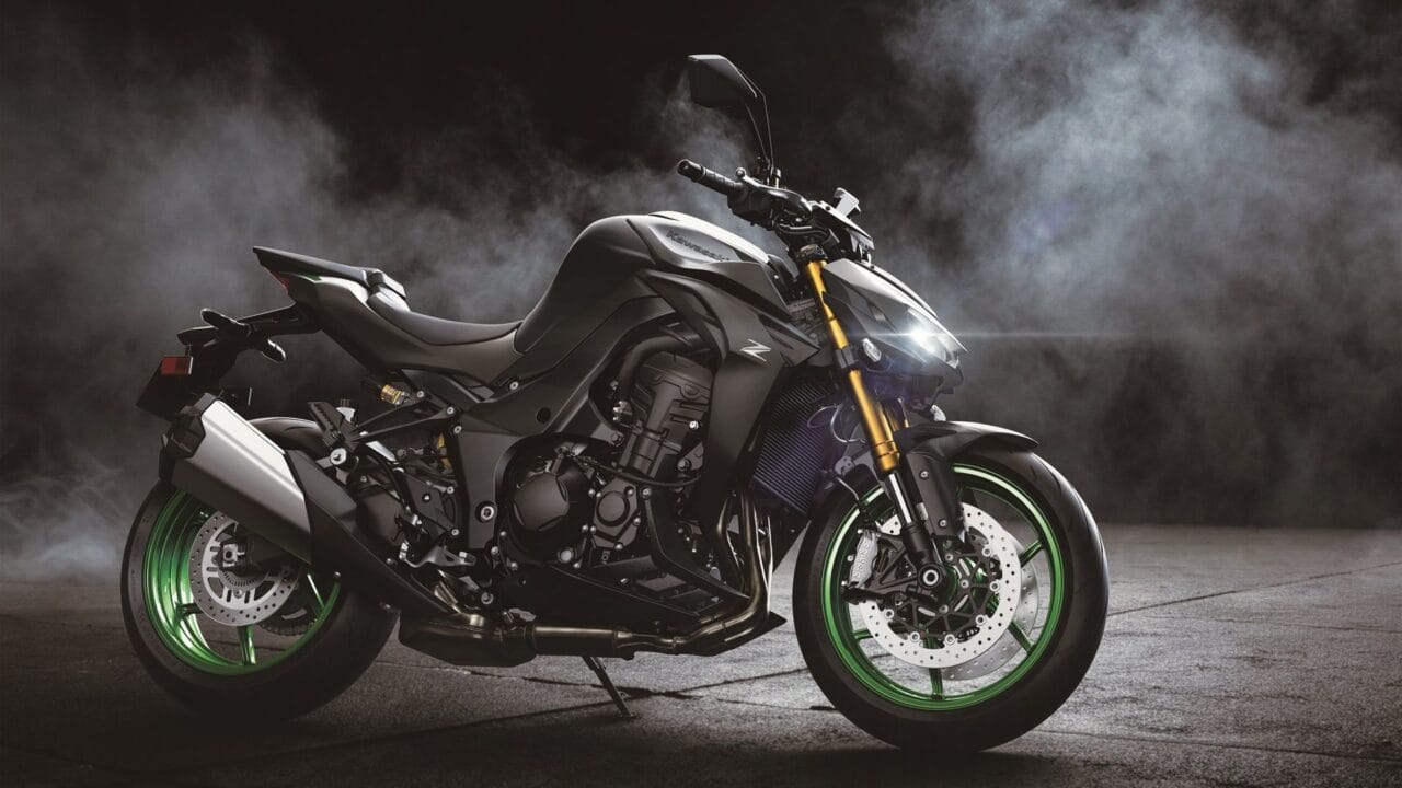 Sport motorcycle (Kawasaki) with black body and bright green rims, front headlight on in a smoky studio setting