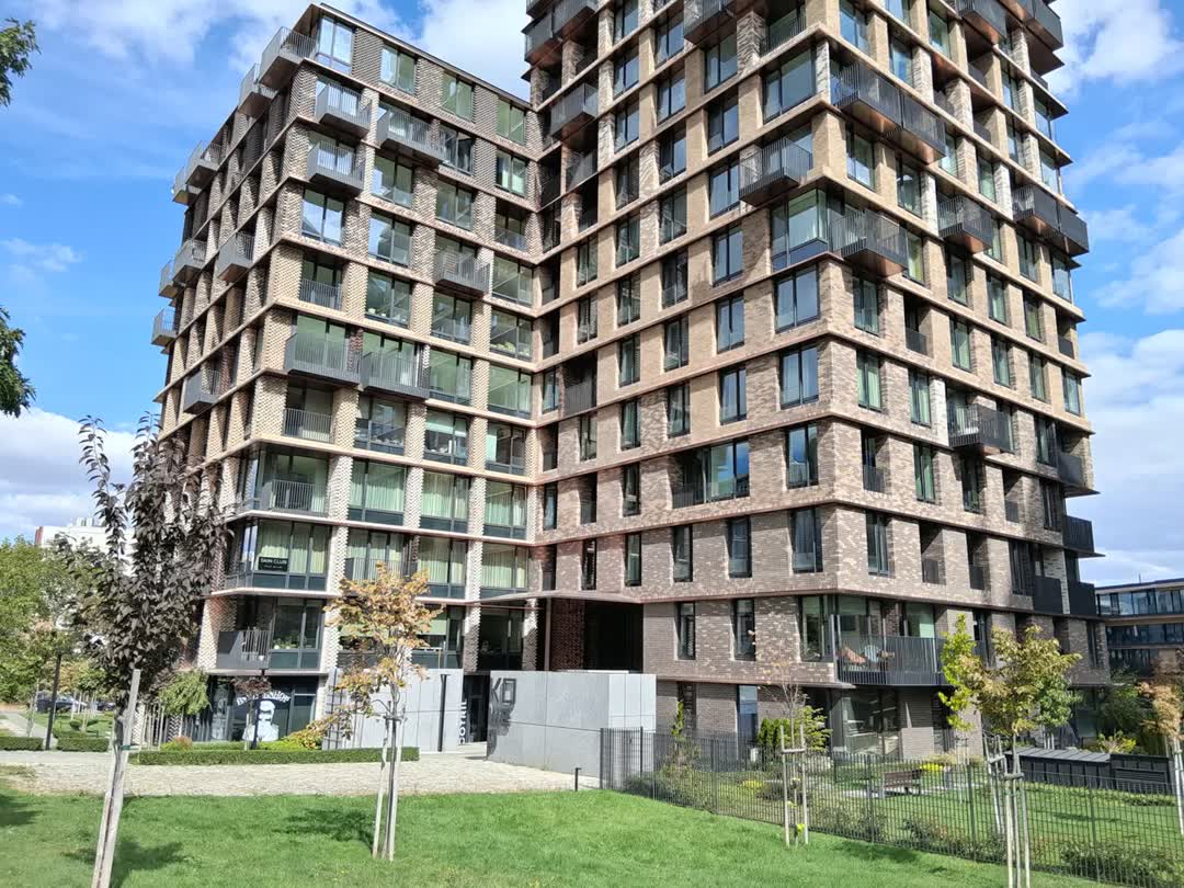 Modern brick apartment building with repeating balconies surrounding a grassy courtyard under a blue sky.