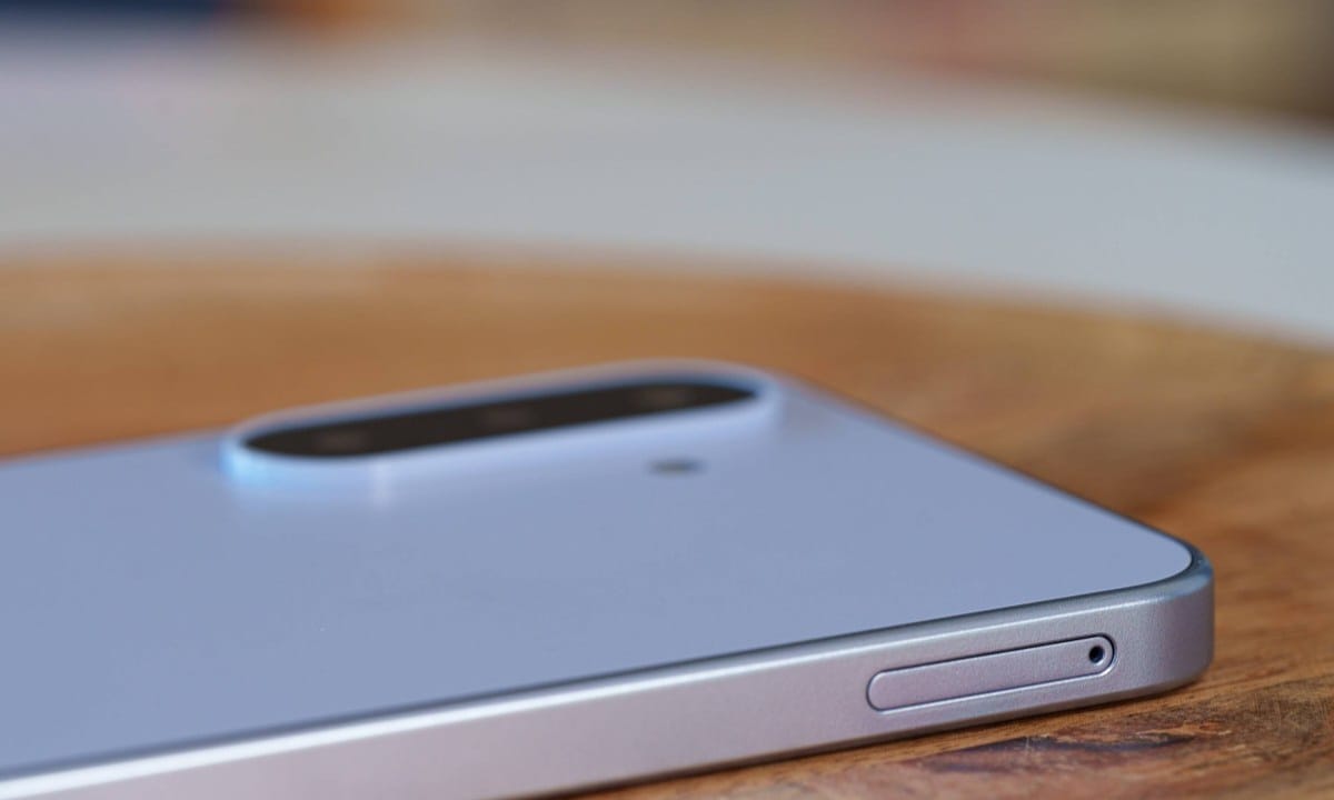 Close-up of a silver smartphone on a wooden table, highlighting its rounded dual-camera bump on the back.