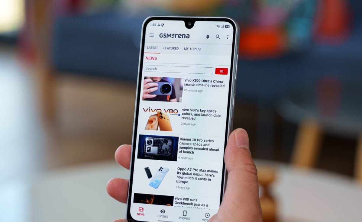 Hand holding a smartphone showing the GSM Arena tech news app with headlines on screen.