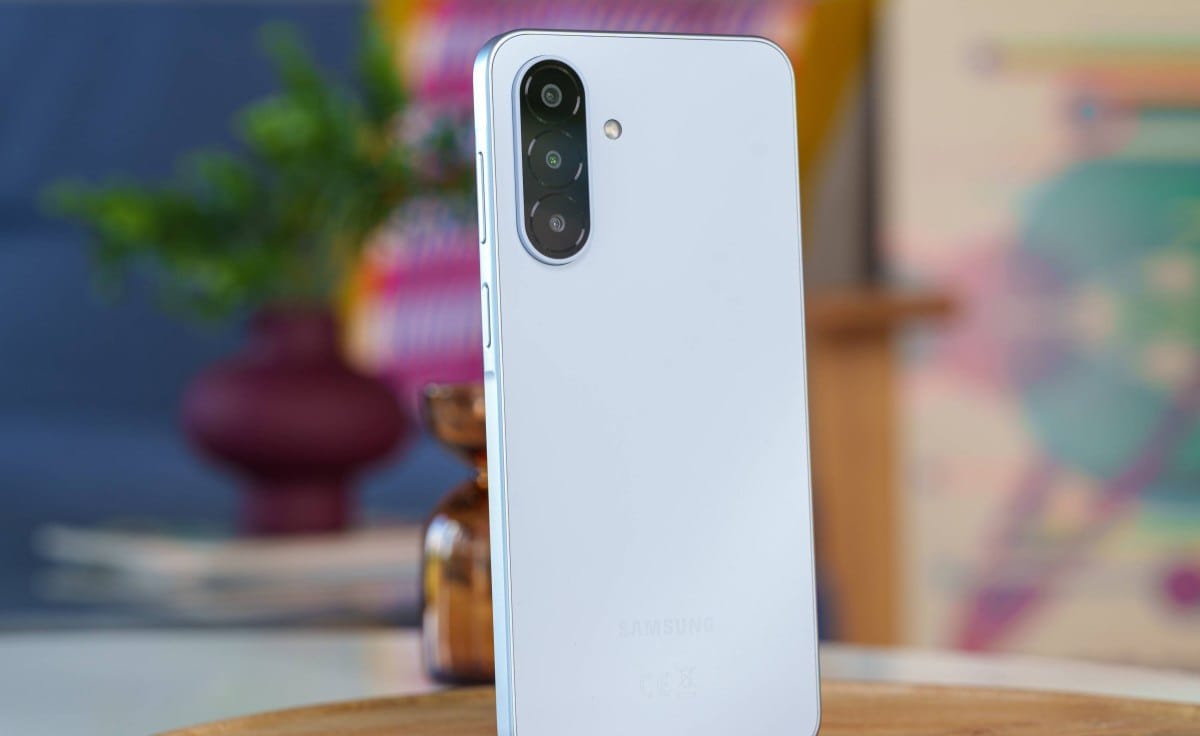 Back of a white Samsung smartphone with a vertical triple-camera array on a wooden table surface