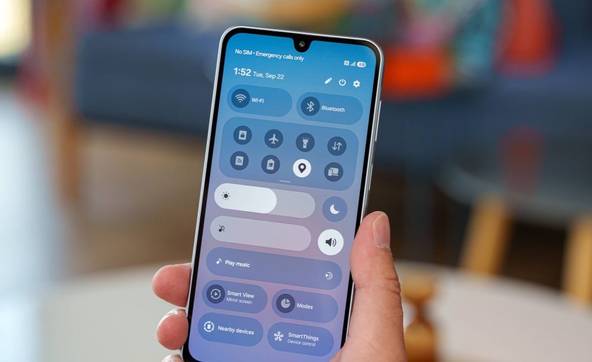Close-up of a hand holding a smartphone displaying a blue control-center with toggles for Wi‑Fi, Bluetooth, brightness, and music icons.