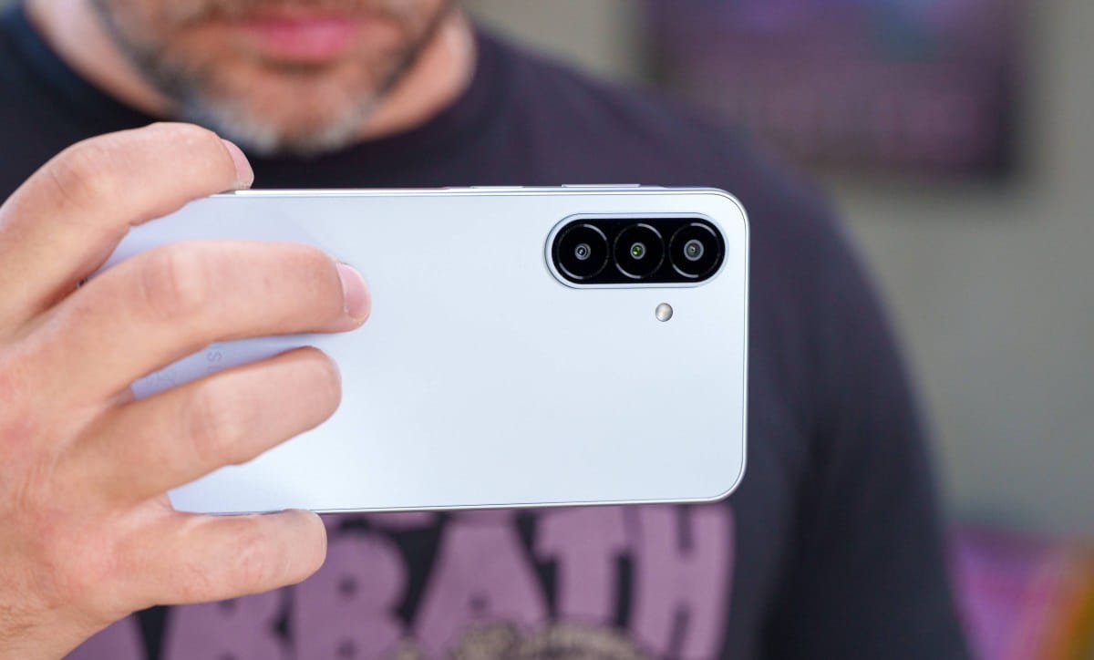 Hand holding a white smartphone showing its triple-camera rear setup and flash on the back.