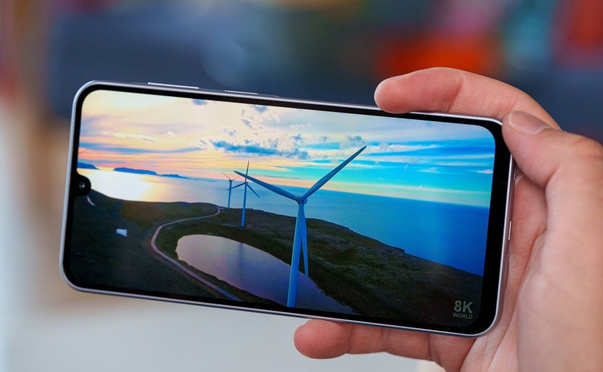 Hand holding a smartphone displaying a coastal landscape with wind turbines at sunset/deserted coast.