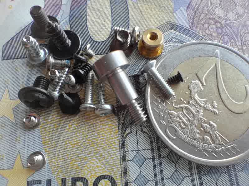 Assorted screws, bolts, and fasteners scattered on a 1-euro coin and euro banknote for scale.