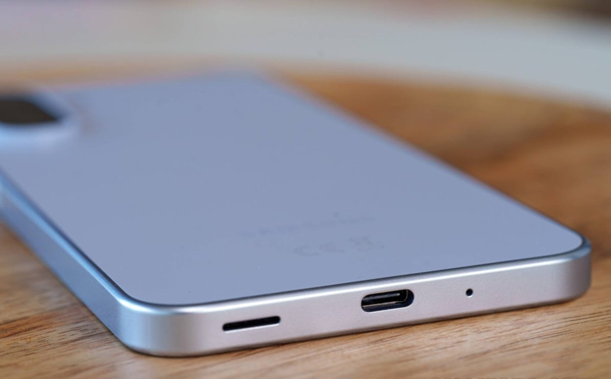 Close-up of a silver smartphone lying on a wooden surface, showing the bottom edge with a USB-C port and speaker grille.