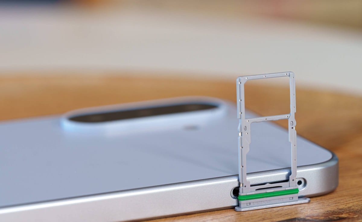 SIM card tray ejected from a silver smartphone lying on a wooden table surface