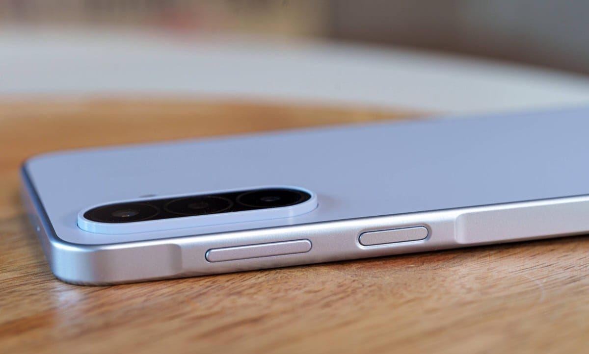 Close-up of a silver smartphone on a wooden surface, highlighting its triple-camera rear module and side buttons