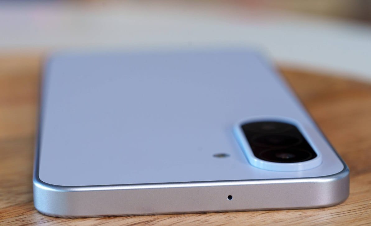 Rear view of a silver smartphone on a wooden table, with a large rectangular camera module in the top-right corner.