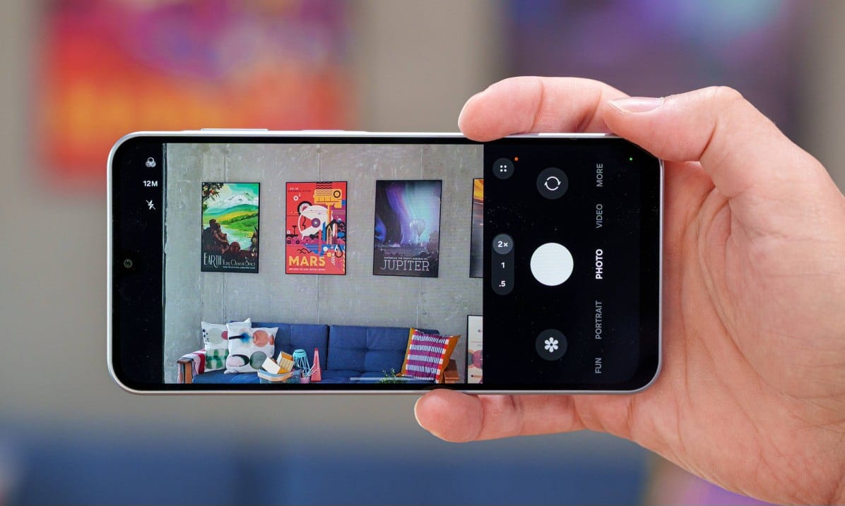 Hand holding a smartphone horizontally, filming a living room with colorful posters on the wall above a blue couch.