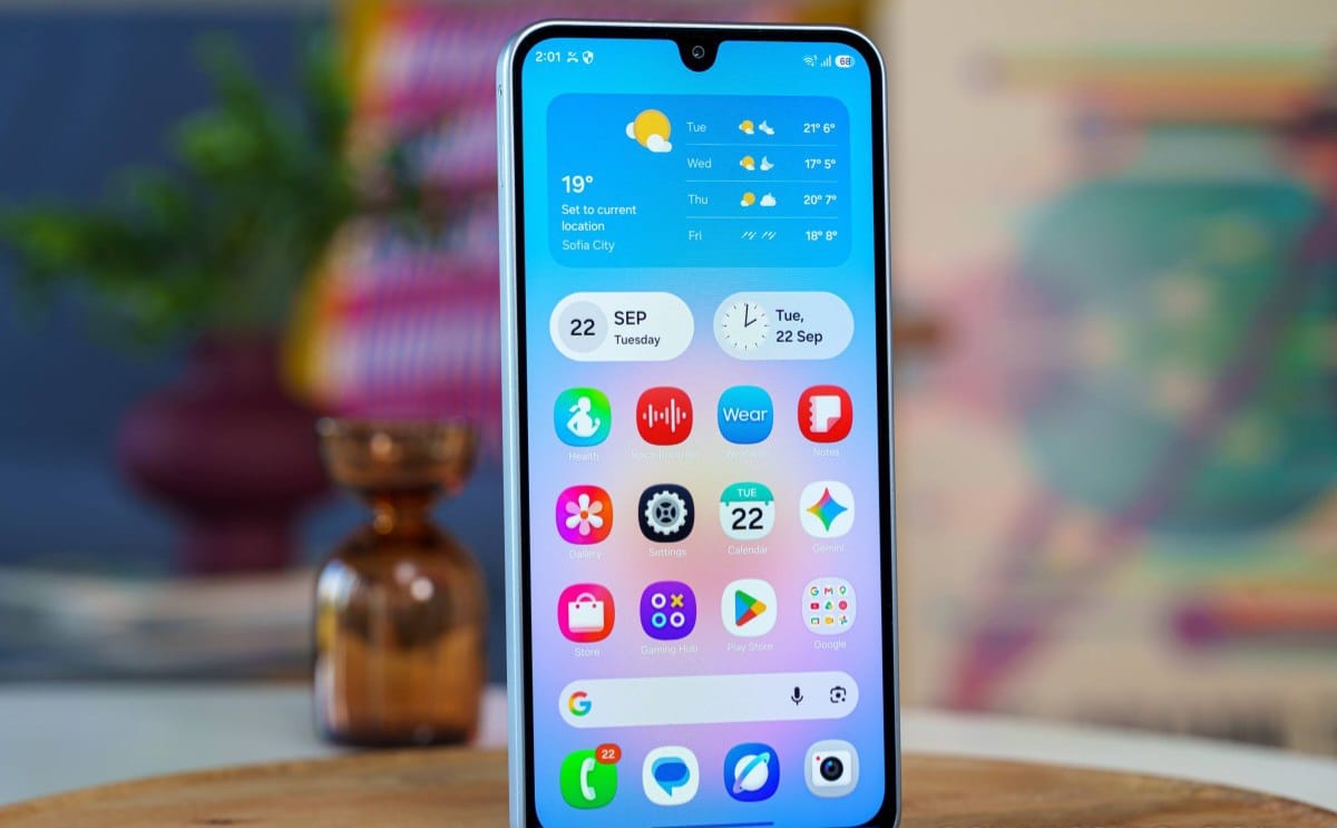 Smartphone on a wooden table showing its colorful home screen with weather widget and app icons in a grid.