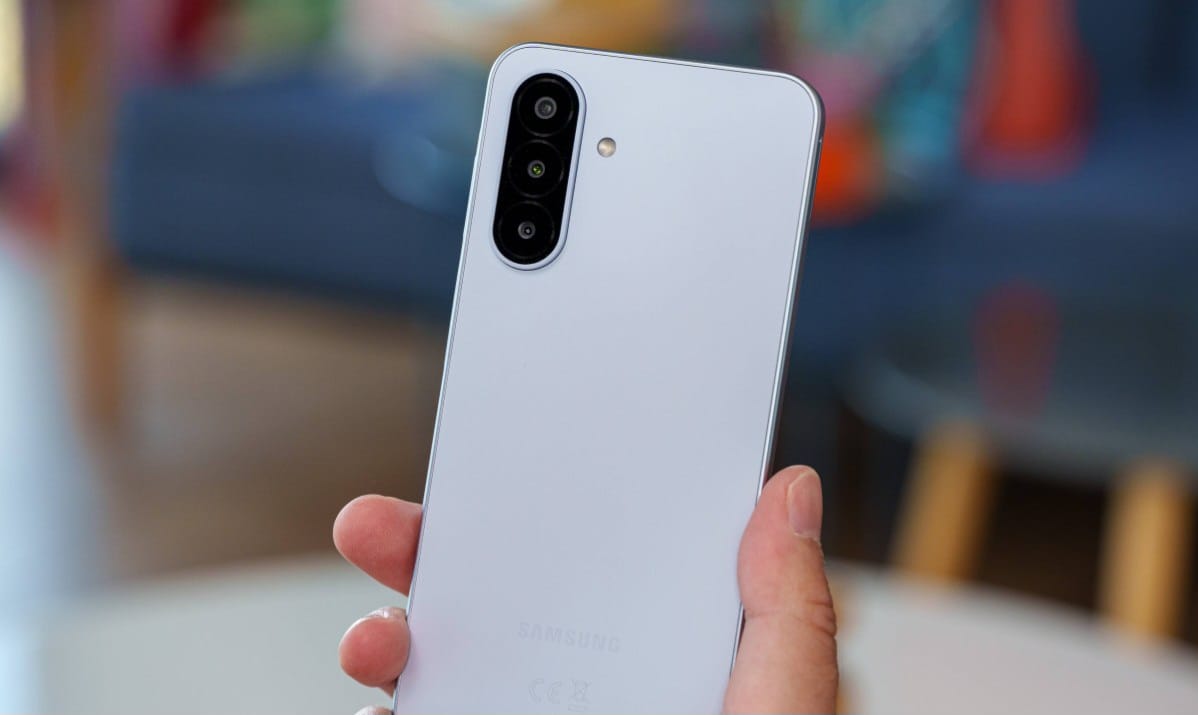 Person holding a white Samsung smartphone showing its vertical triple-camera setup on the back.
