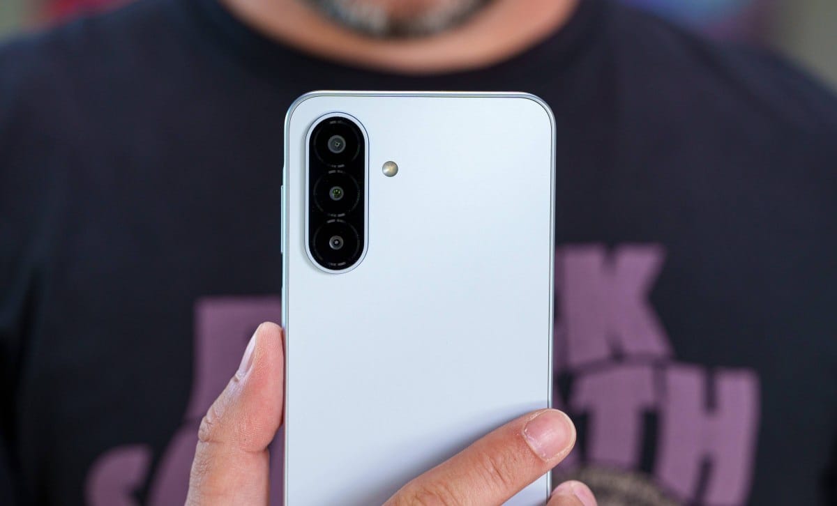 Back of a silver smartphone showing a vertical triple-camera array being held by a hand in foreground.