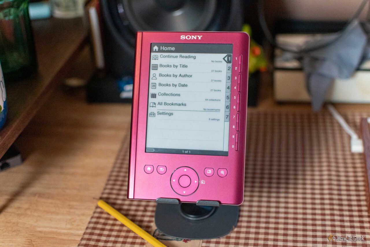 Pink Sony e-reader displaying its menu: Home, Continue Reading, Books by Title, Books by Author, and more on a desk.