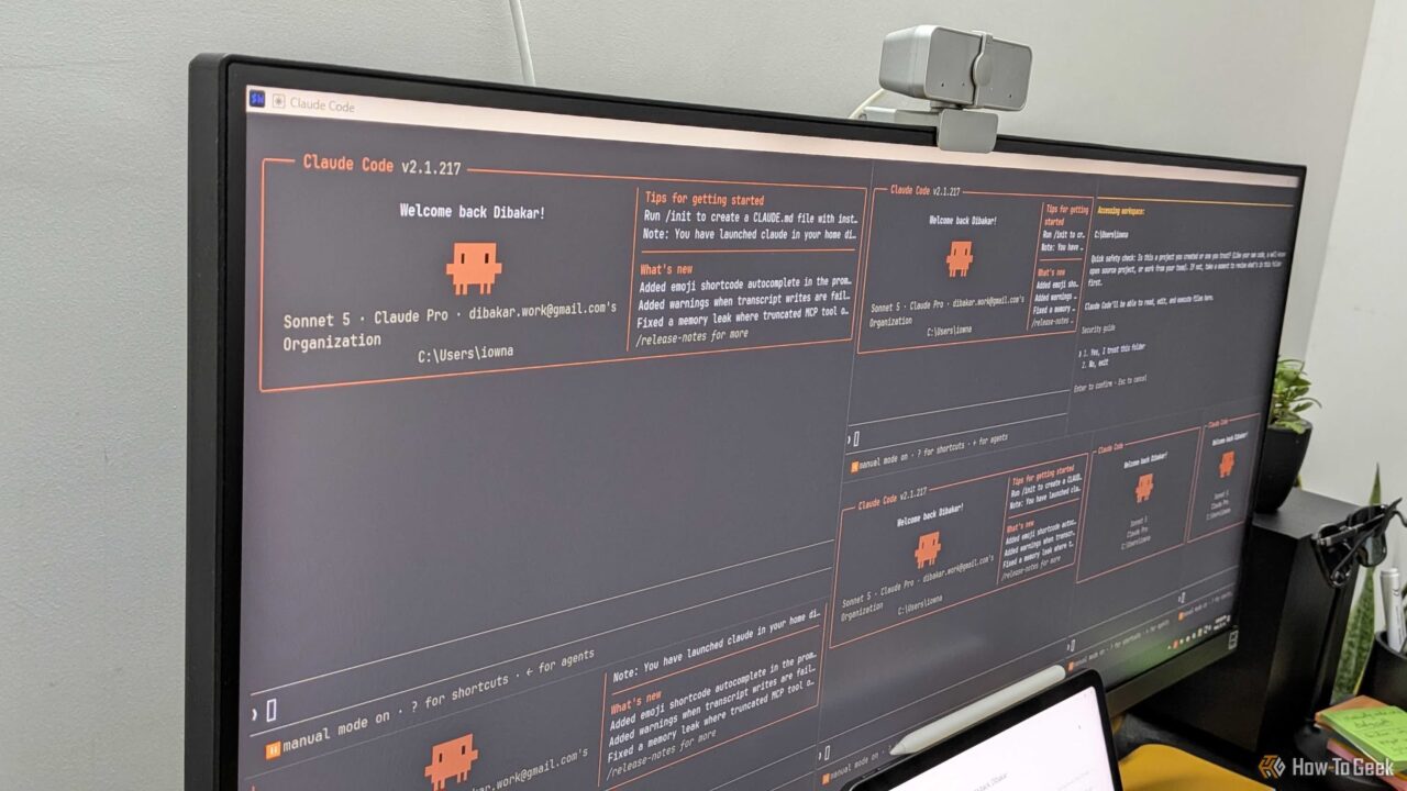 Monitor displaying Claude Code interface with orange text on dark panels and a small pixel robot icon in the center-left area.