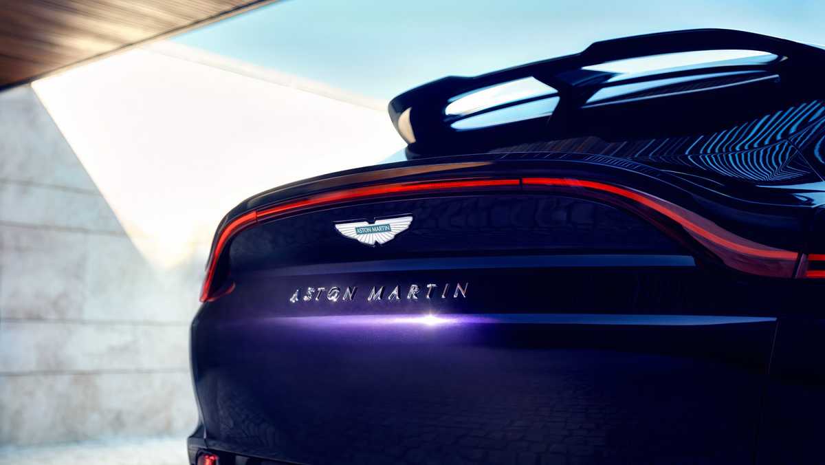 Rear view of a glossy black Aston Martin sports car with a red taillight arc and badge on the trunk.