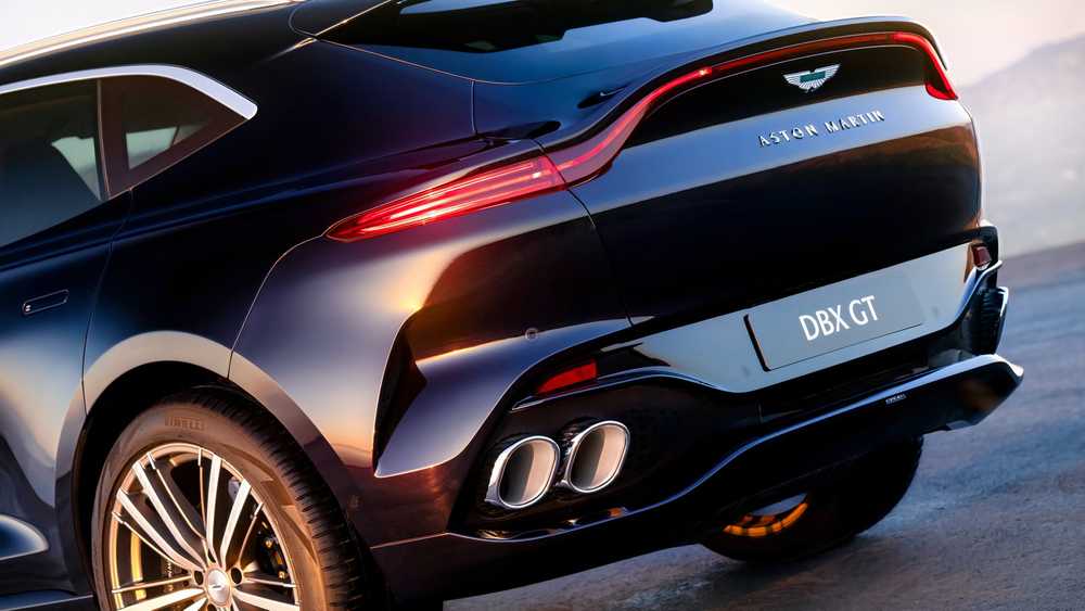 Rear view of a glossy black Aston Martin DBX GT SUV, with curved taillights and quad exhausts visible at the rear cap.
