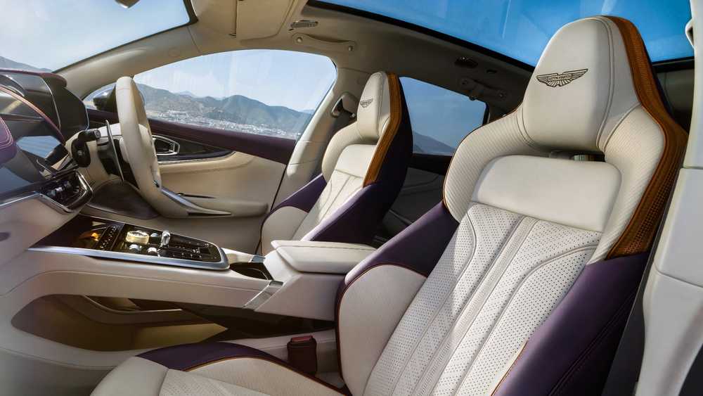 Interior of a luxury car with cream leather seats, purple accents, and a center console; Aston Martin branding on headrests.