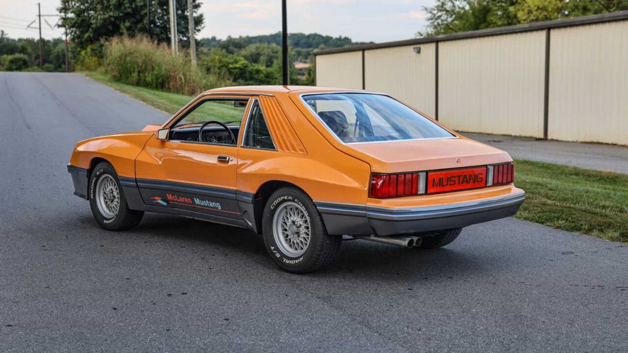 Orange classic Ford Mustang viewed from the rear three-quarter, parked on a street.