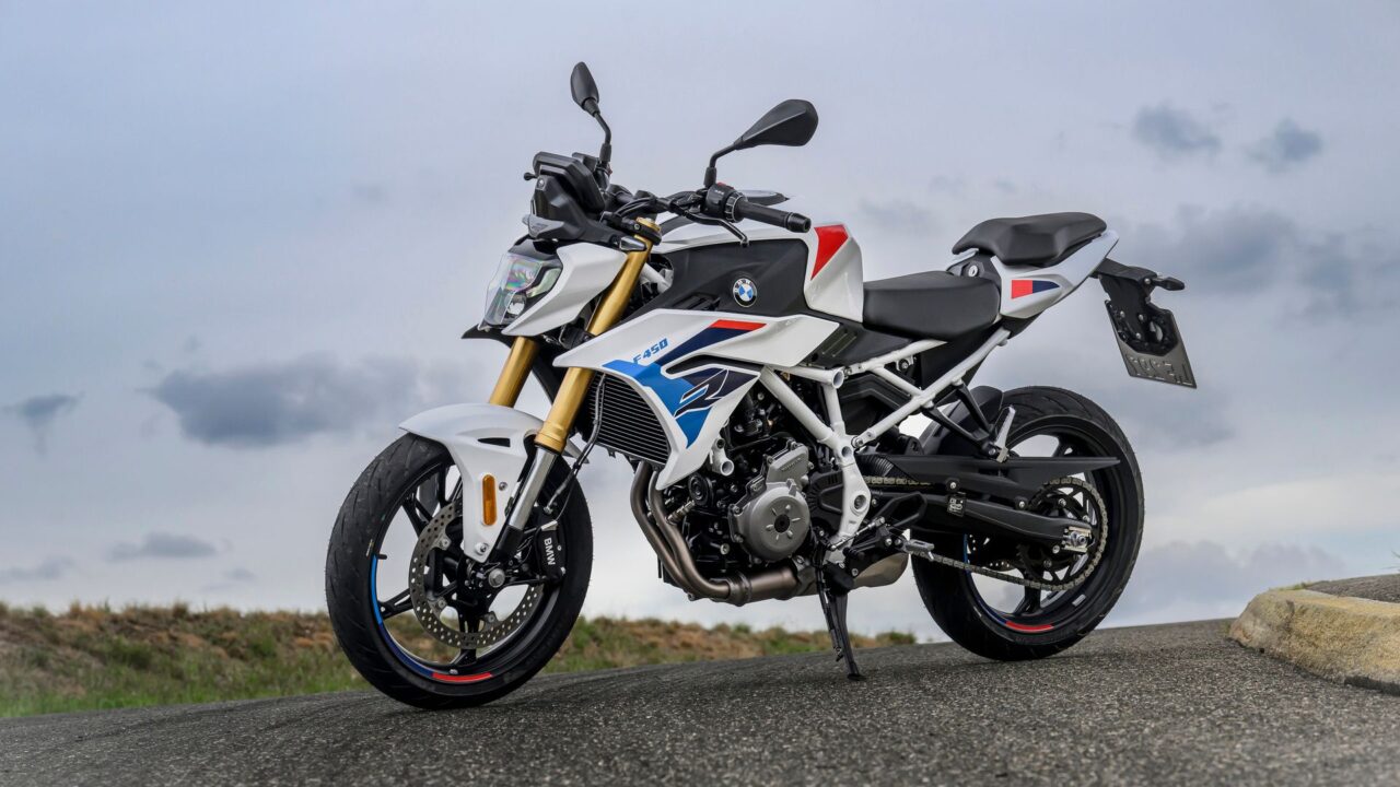 White BMW sport motorcycle on a road with a cloudy sky, featuring gold front forks and blue/red graphics on the fairing.
