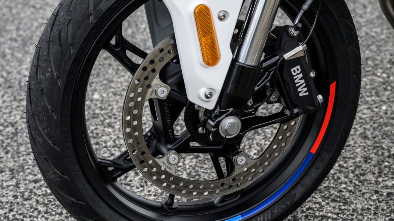 Front wheel of a motorcycle showing a drilled brake disc, black Brembo caliper with BMW logo, white fork leg and orange reflector.