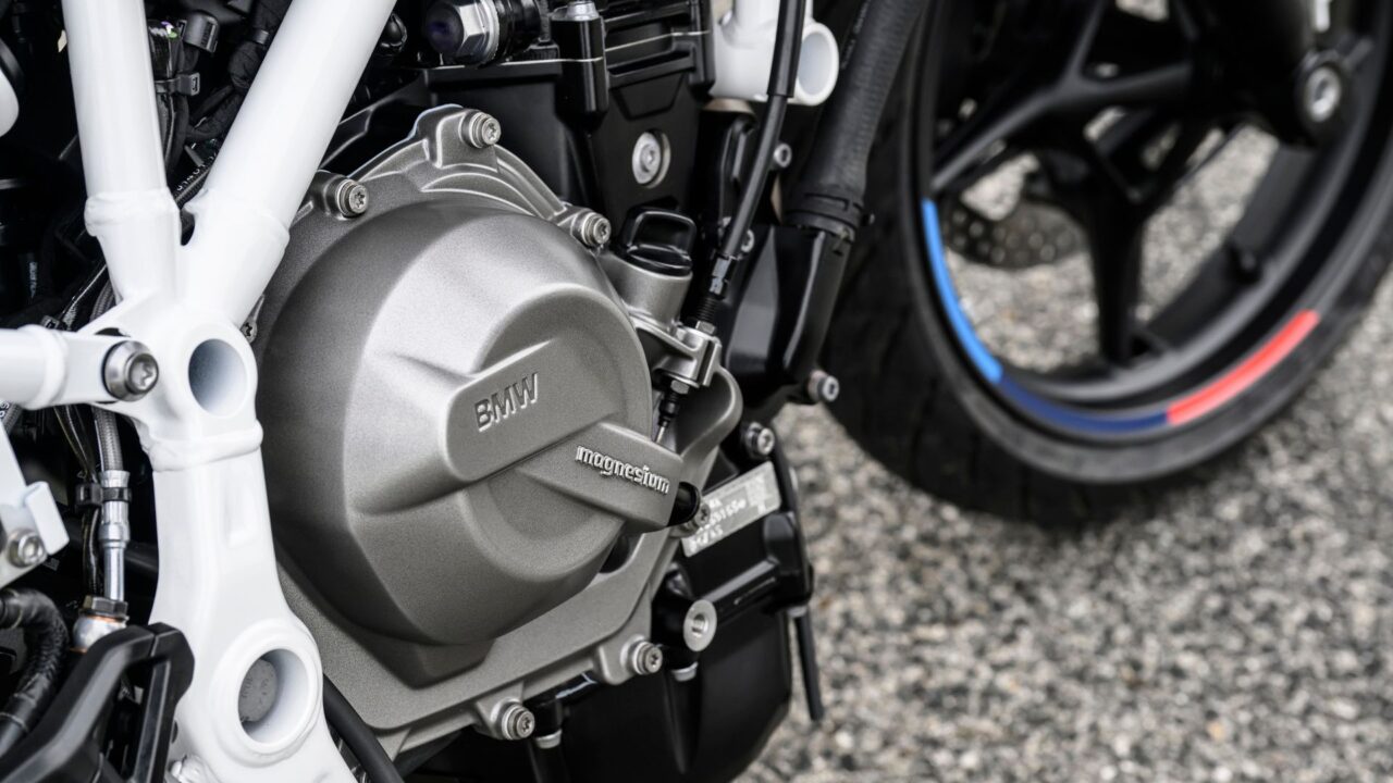 Close-up of a BMW motorcycle engine casing with 'magnesium' label, white frame, and a wheel with blue and red accents visible in the background.