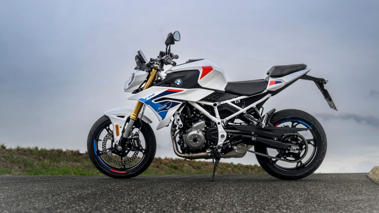 White BMW motorcycle with blue and red decals, shown in a side view parked on a road edge.