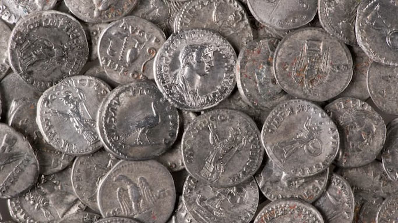 Close-up of a pile of worn silver coins with various designs and portraits