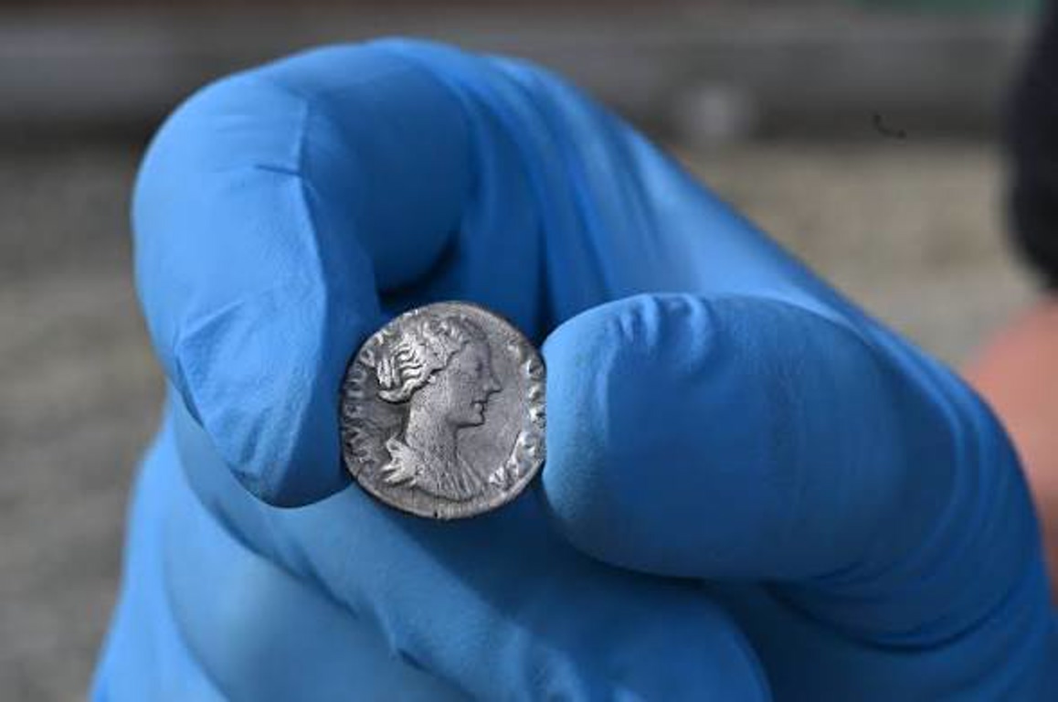 Close-up of a gloved hand holding a small silver coin (a U.S. dime) between the thumb and index finger.