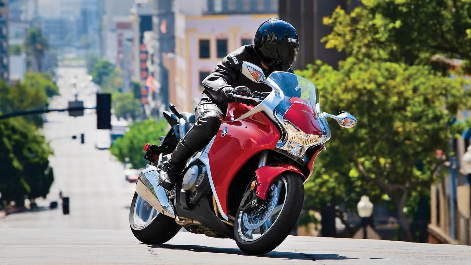 Rider in black gear and helmet leaning into a sharp red Honda sport motorcycle on an urban street.