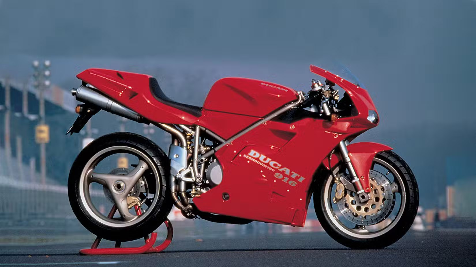 Red Ducati sport motorcycle on a rear stand on a race track backdrop, ready for maintenance or display