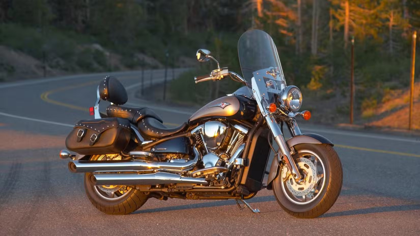 Chrome touring motorcycle with leather saddlebags and tall windshield parked on a winding road at golden hour sunset