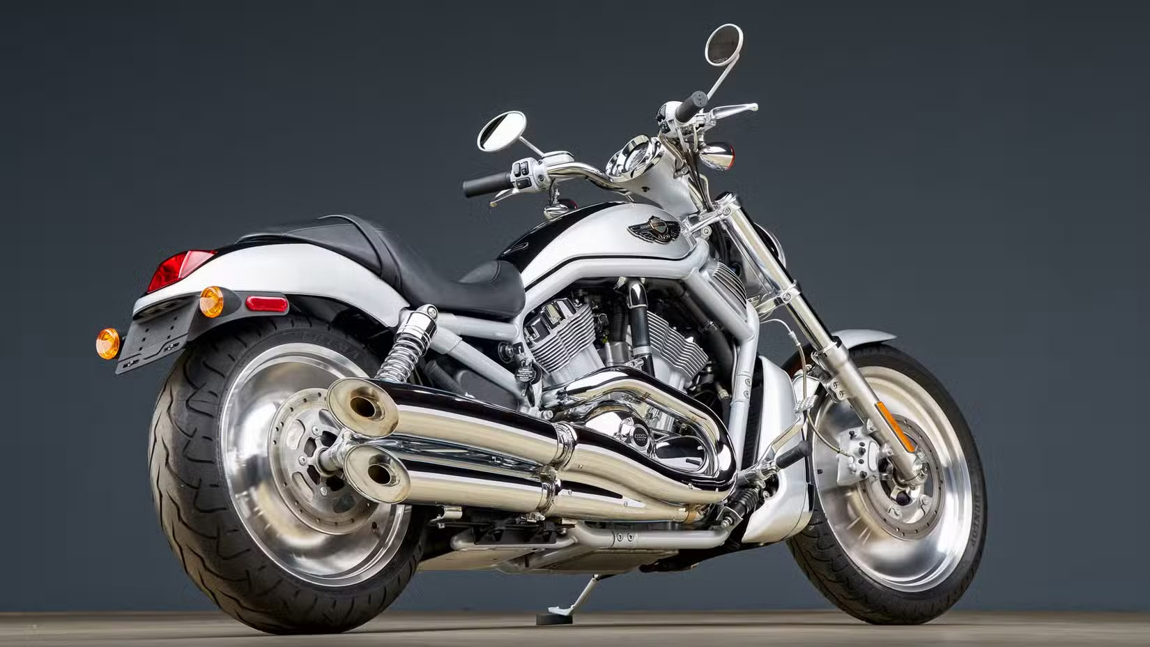 Silver chrome motorcycle photographed from the left-rear side, parked on a flat surface against a dark gradient background.