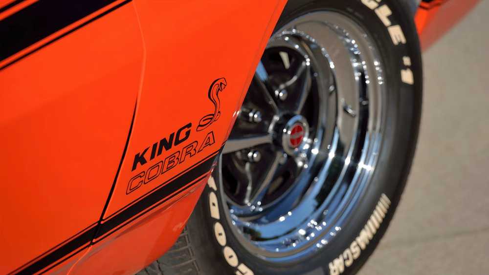 Orange car side panel with a 'King Cobra' emblem and a snake logo, beside a chrome wheel and tire edge.