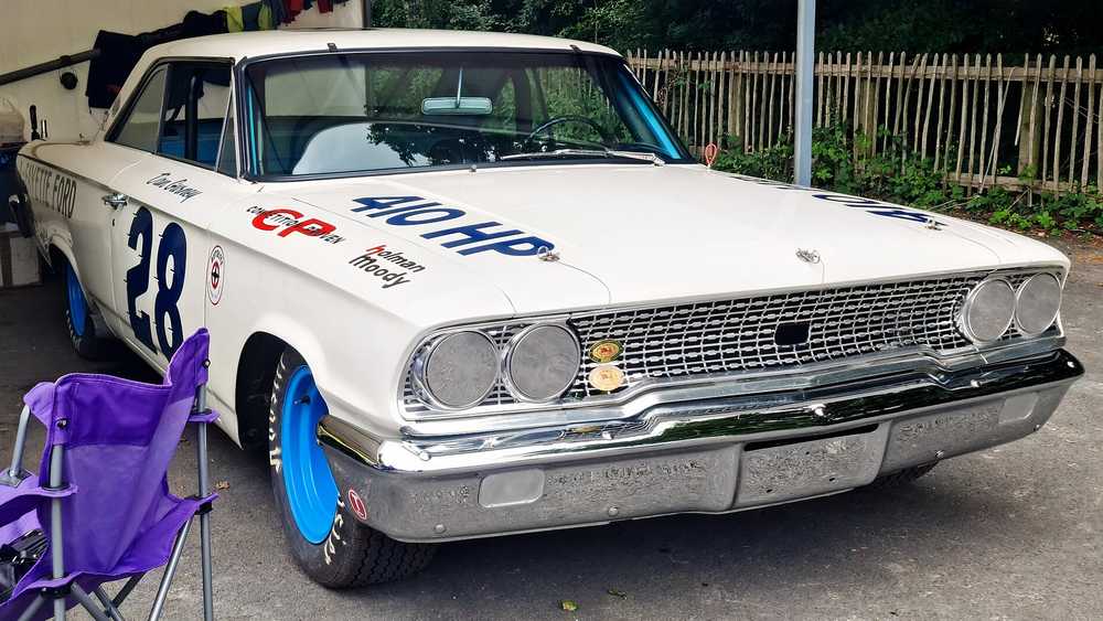 White vintage race car with blue wheels and large number 28 on the door, parked in a driveway with a purple lawn chair nearby.