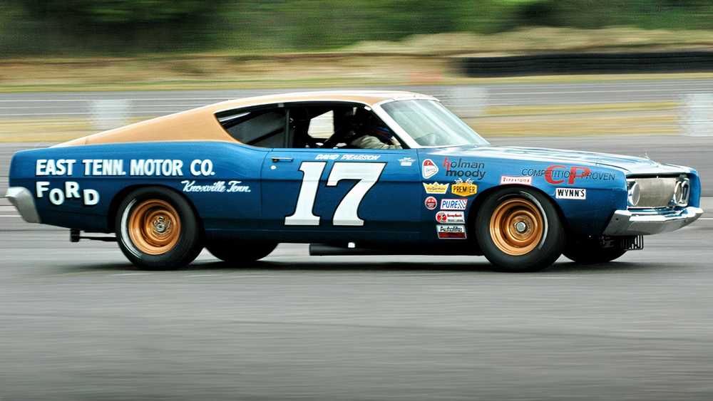 Blue vintage race car with orange roof and large white number 17 speeding along a race track on a blurred background.