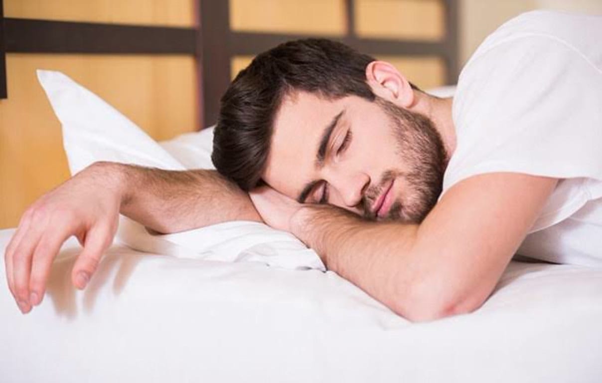 Man with dark hair and beard sleeping on a white pillow on a bed in a bedroom