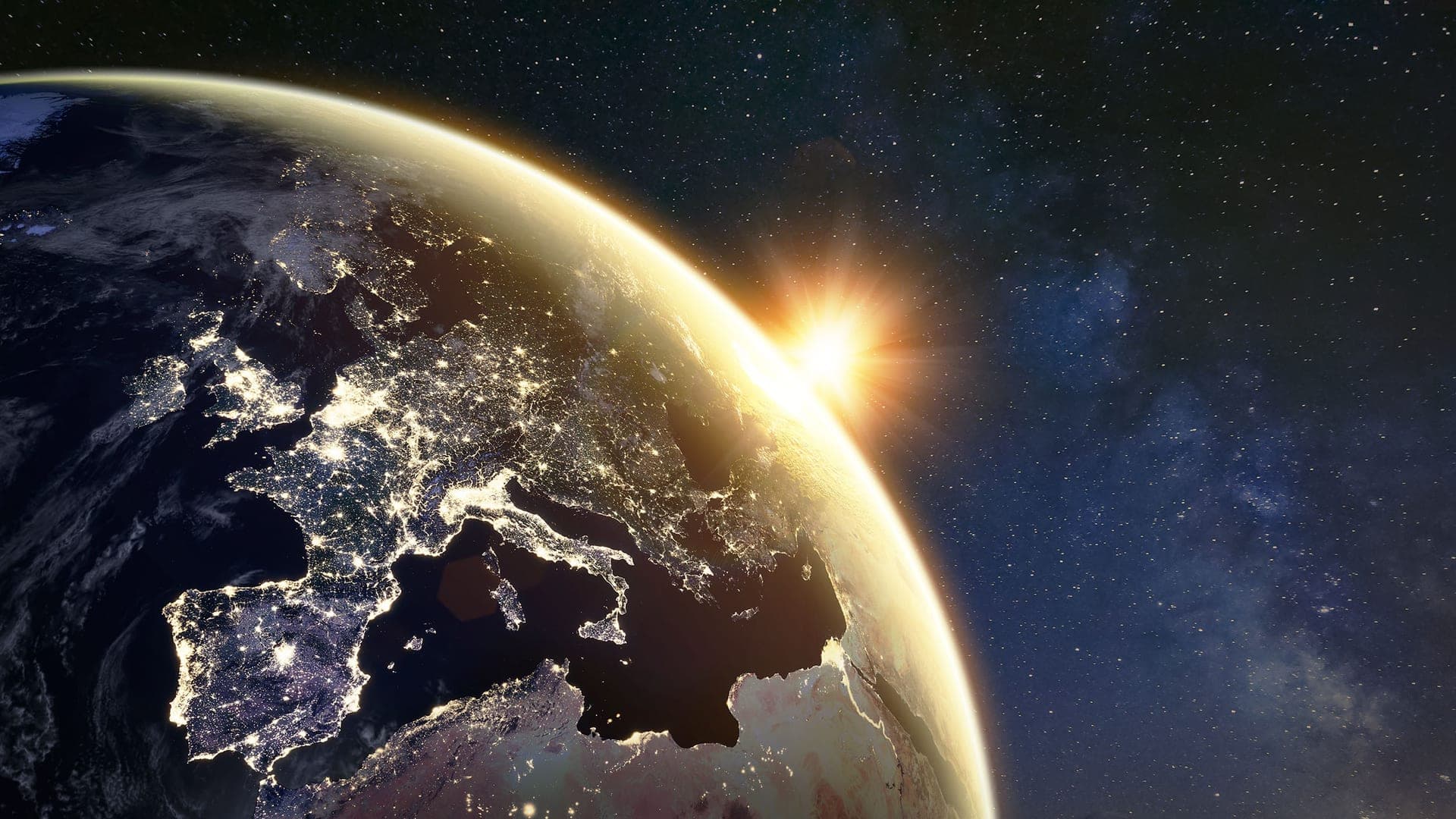 Earth seen from space with the sun rising over the horizon, city lights visible on the dark side.