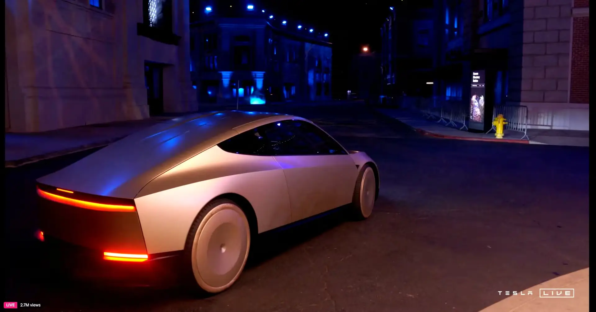 White futuristic sedan (Tesla) driving on a dim street at night with blue neon lighting, rear red taillights visible and 'TESLA LIVE' watermark in corner