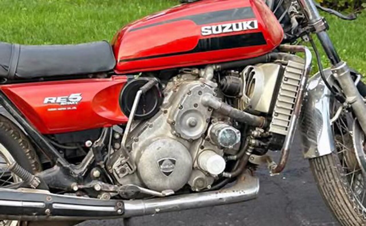 Red Suzuki motorcycle side view showing the exposed engine and chrome exhaust pipes on a paved surface.