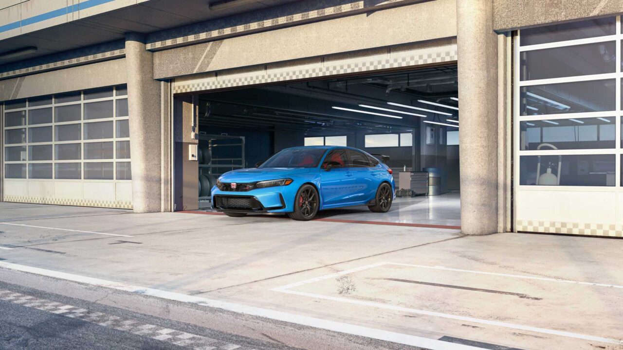 Bright blue sports car parked inside an industrial garage with open bay doors, concrete pillars and overhead lighting.]','Blue performance sedan inside a gray automotive workshop, visible front grille and dark wheels.