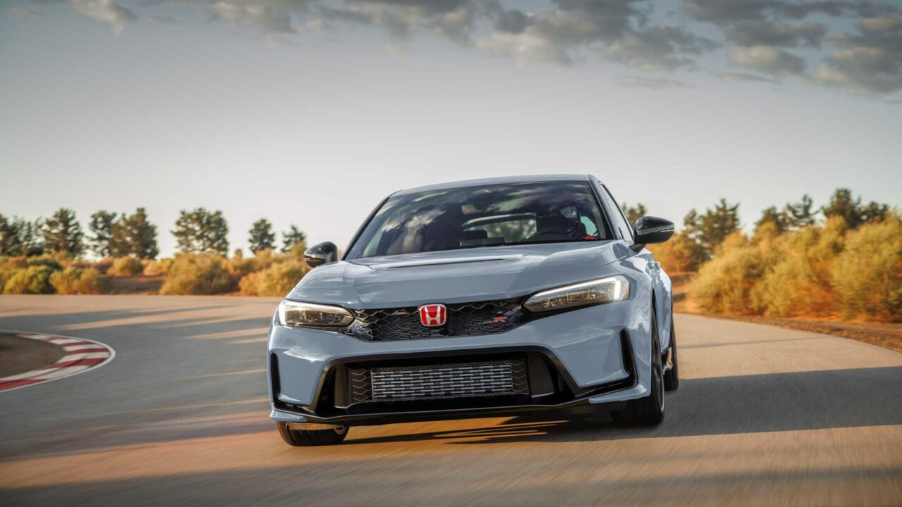 Front view of a silver Honda Civic Type R speeding on a racetrack with autumn trees in the background.