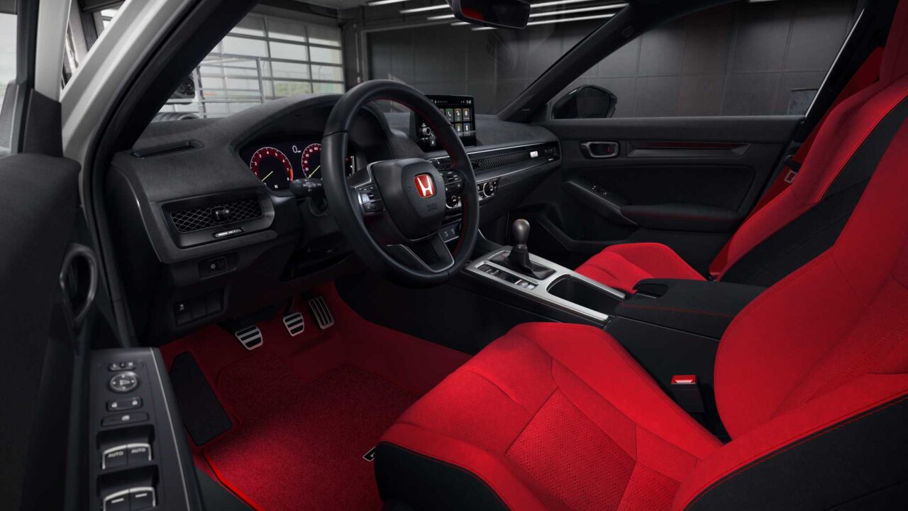 Interior of a sports sedan with red leather seats, black dashboard, and a center console showing a touchscreen display and gear shifter under bright lighting.