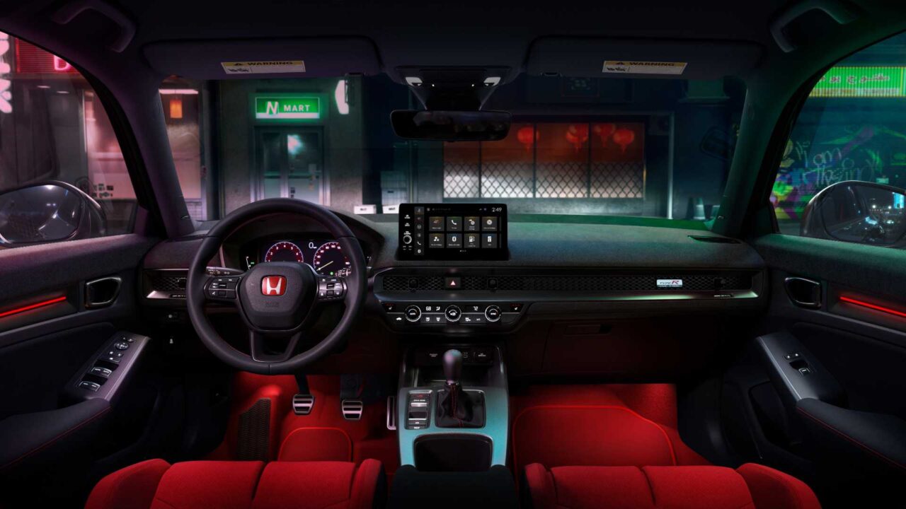 Interior of a modern car at night viewed from the back seat, red seats, illuminated dashboard and center touchscreen, neon city streets outside with signs visible through windshield