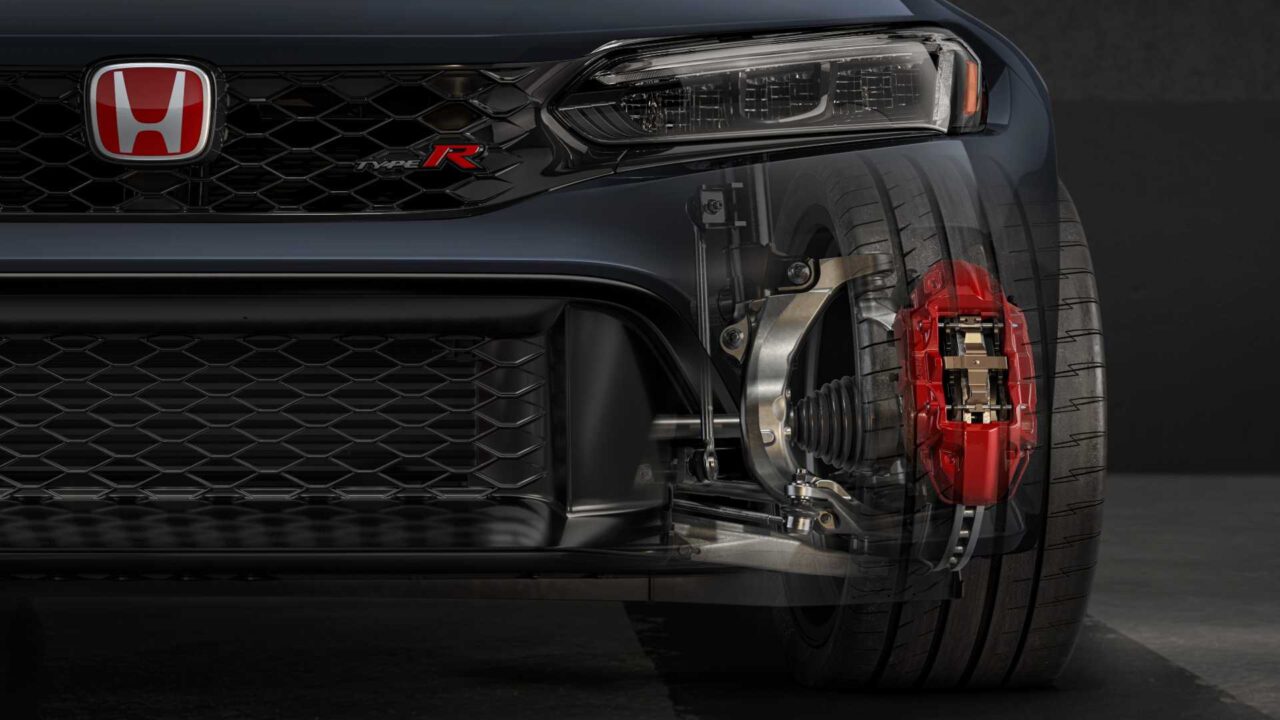 Close-up of a Honda front end showing the grille, headlight, and a cutaway view of the front wheel with a red brake caliper and exposed suspension components behind the tire.