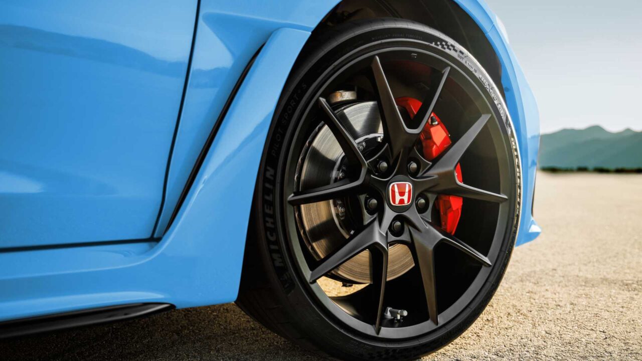 Close-up of a blue sports car wheel with a black alloy rim, red brake caliper, and disc brake visible.