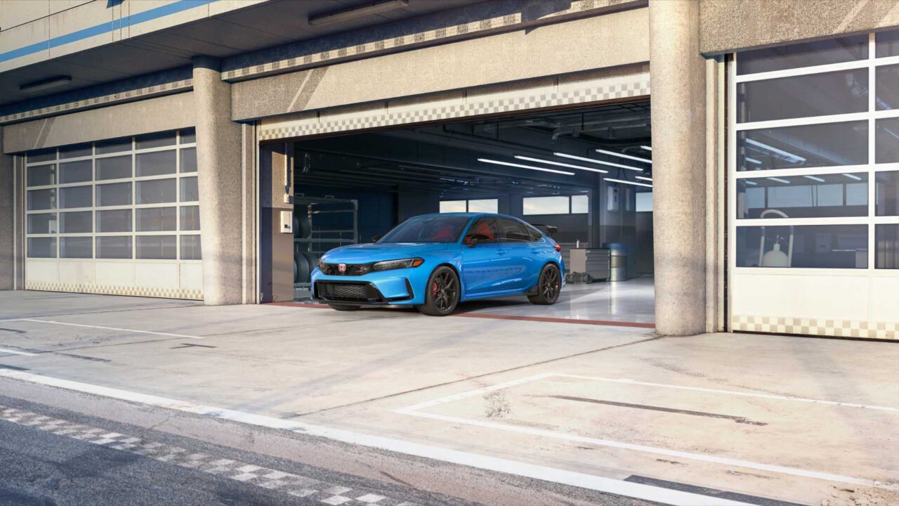 Blue sports sedan parked in an open garage bay at a race track, with red brake calipers and dark wheels.
