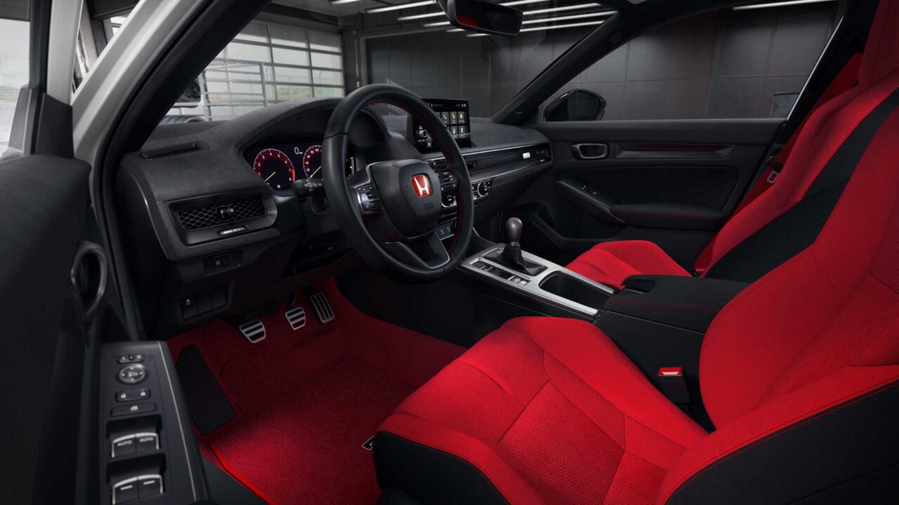 Sporty car interior featuring bold red seats and black dashboard, with a center touchscreen and manual gear shifter visible.